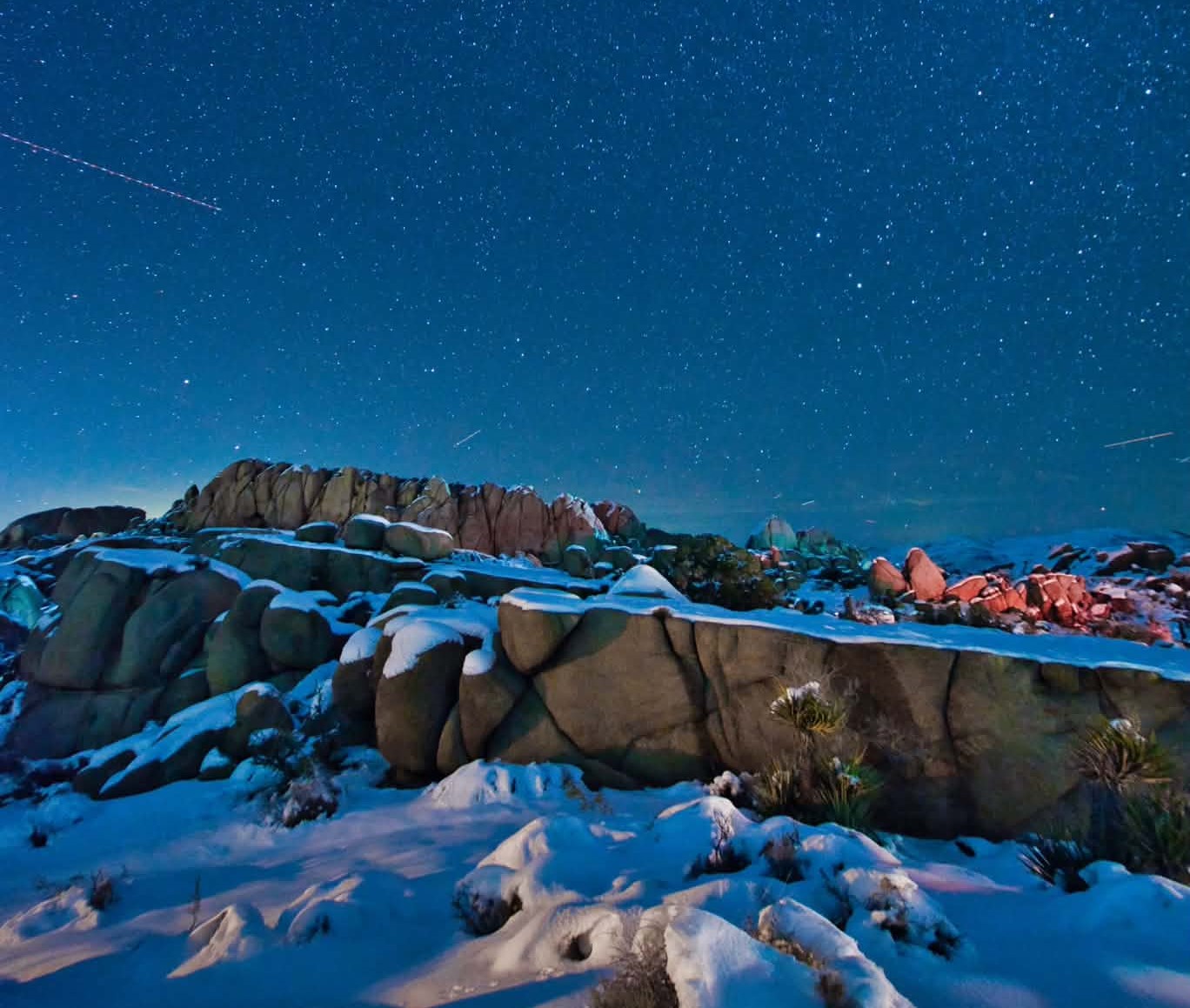 Snow-covered boulder formations beneath a star-filled night sky.